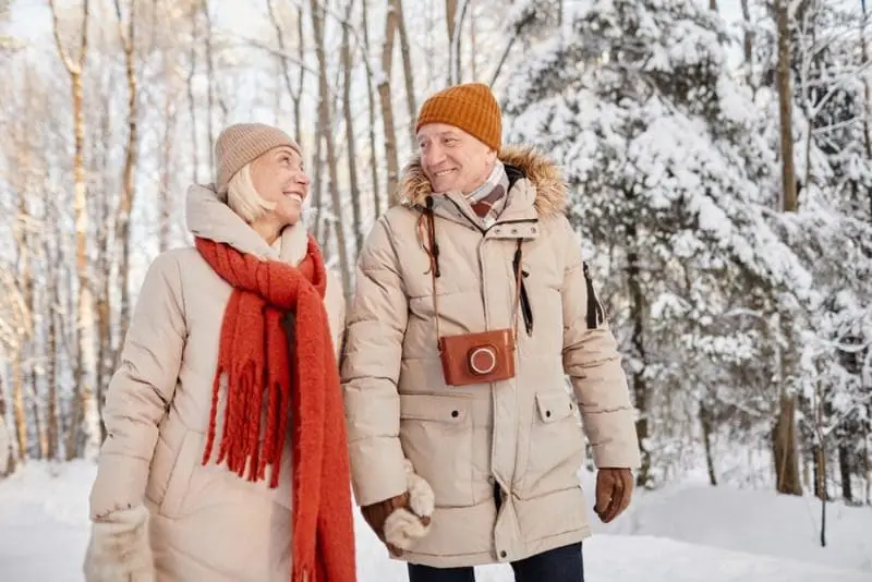 A senior couple smiles at each other as the walk around a snow-covered forest during a Nova Scotia winter getaway.
