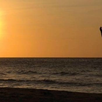 man doing yoga on a beach at sunrise