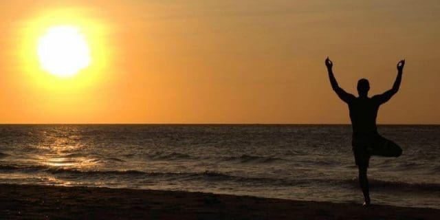 man doing yoga on a beach at sunrise