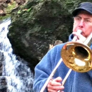 Dr Paul playing trombone next to a waterfall