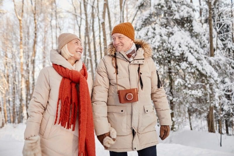 A senior couple smiles at each other as the walk around a snow-covered forest during a Nova Scotia winter getaway.