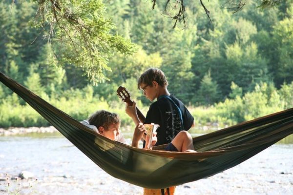 Stay-Camping young people. one standing with a guitar. one in a hammock by Indian Brook.